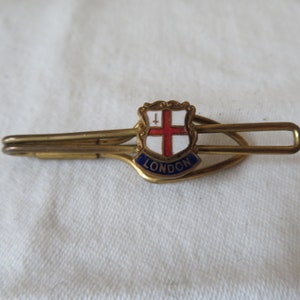 May include: A gold tie clip featuring a red cross on a white shield with the word "LONDON" underneath.