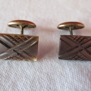 May include: A pair of brown and black cufflinks with a geometric design. The cufflinks have a gold-toned metal backing.