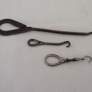 Könnte beinhalten: Drei antike Schnallenhaken aus Metall. Der größte Haken ist mit "Shines Fine Produced Size" beschriftet.