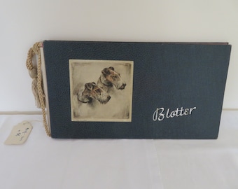 May include: A blue leather-bound blotter with a tassel. The front cover features a drawing of two wirehaired fox terriers. The text "Blotter" is embossed in silver on the front cover.