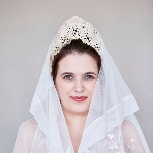 May include: A woman wearing a white veil with floral embroidery and a white lace crown.