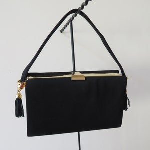 May include: A black evening bag with a gold clasp and tassel accents. The bag has a long strap and is made of a soft, textured fabric.