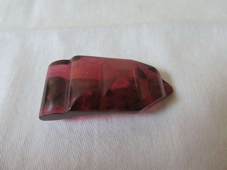 May include: A deep red, faceted, glass button with a pointed end.