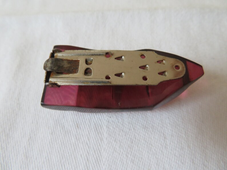 May include: A vintage purple plastic iron with a metal base and a spring-loaded clip. The iron has a textured surface and a pointed tip.