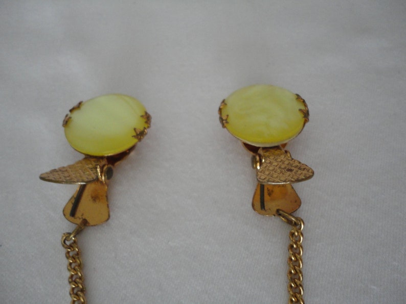 May include: A pair of gold-tone collar clips with a chain connecting them. Each clip features a round, pale yellow, translucent stone.