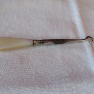 May include: A silver shoe horn with a white mother-of-pearl handle.