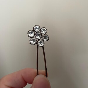 May include: A silver hair pin with a flower-shaped design featuring seven clear rhinestones.