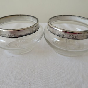 Puede incluir: Dos saleros de vidrio transparente con bordes de plata. Los bordes de plata están marcados con las letras "925" y "(sterling)".