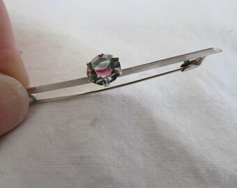 May include: A silver brooch with a round, multi-colored gemstone in the center.