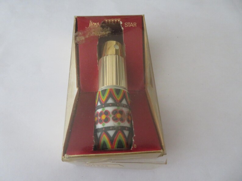 May include: A vintage perfume bottle in a box. The bottle has a gold-colored top and a patterned design with flowers and geometric shapes in red, yellow, green, and black. The box is red and gold.
