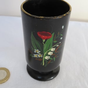 Puede incluir: Jarrón de madera negro con un diseño floral pintado a mano. El jarrón presenta una amapola roja, flores blancas y hojas verdes.