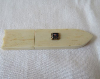 May include: A small, ivory-colored, two-piece letter opener with a gold-colored, square-shaped, decorative piece in the center. The decorative piece has a blue background with a small, pink flower design.