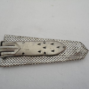 May include: A silver metal belt buckle with a geometric design and a mesh backing.