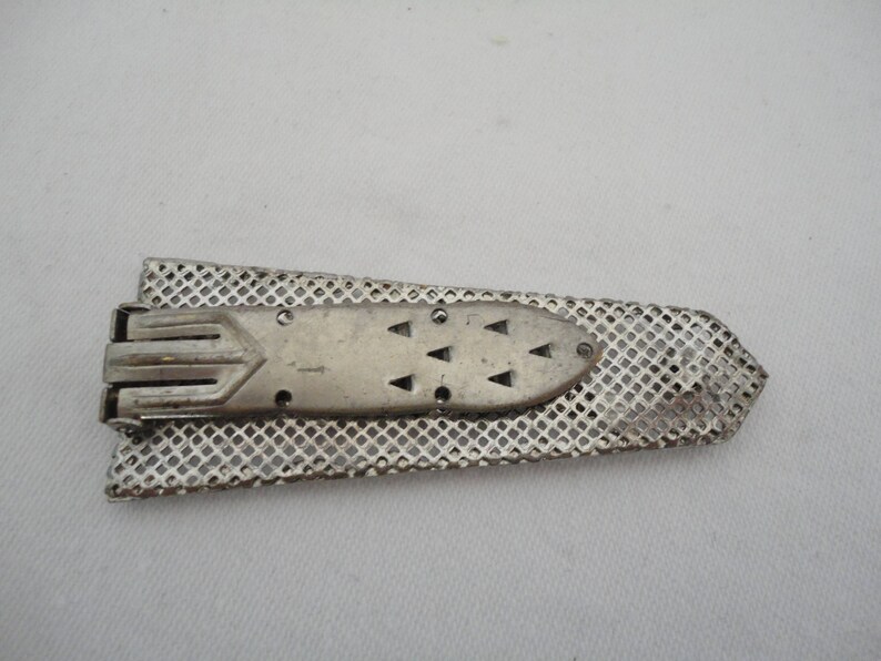 May include: A silver metal belt buckle with a geometric design and a mesh backing.