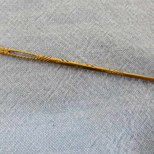 Pode incluir: Um passador de agulha dourado vintage com desenhos gravados intrincados. A ferramenta apresenta um corpo longo e fino com um pequeno orifício para enfiar agulhas. Este passador de agulha é uma ferramenta de costura.