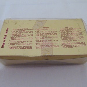 May include: A vintage atomizer in a clear plastic case. The box is yellow with instructions in multiple languages. The text "Made in West-Germany" is visible. The atomizer is likely for perfume or other liquids.