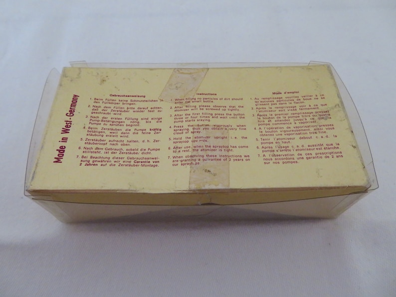 May include: A vintage atomizer in a clear plastic case. The box is yellow with instructions in multiple languages. The text "Made in West-Germany" is visible. The atomizer is likely for perfume or other liquids.