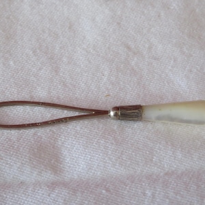 Puede incluir: Una cadena de gafas de plata y madreperla blanca con un bucle en un extremo y un pequeño mango en el otro.