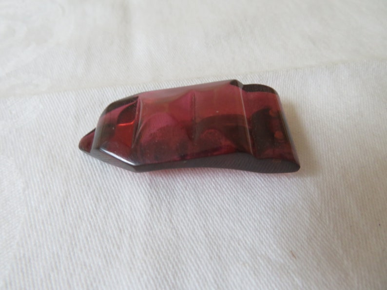 May include: A deep red, faceted, glass pendant with a geometric shape.