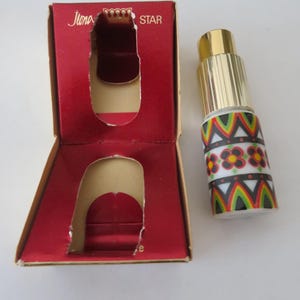 May include: A vintage perfume bottle with a gold cap and a decorative patterned design in red, black, green, and white. The bottle is next to its open red box, which has the words "Ilona Star" printed on it.