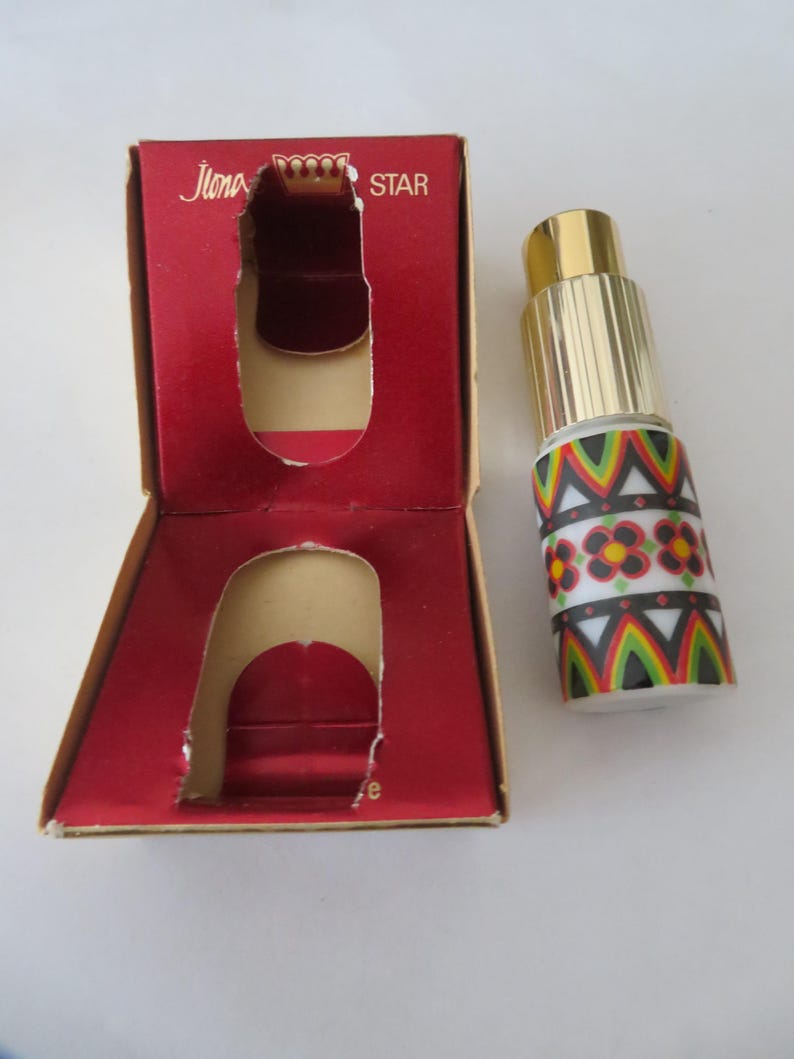 May include: A vintage perfume bottle with a gold cap and a decorative patterned design in red, black, green, and white. The bottle is next to its open red box, which has the words "Ilona Star" printed on it.