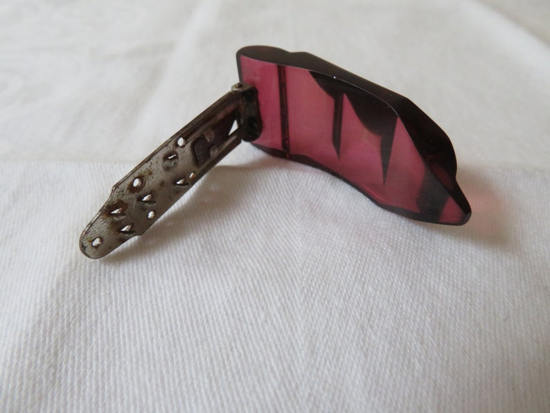 May include: A vintage, dark pink, plastic, hinged hair clip with a silver metal hinge and a decorative, cut-out design.