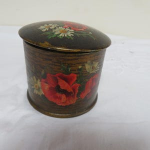 May include: A vintage, cylindrical trinket box with a hinged lid. The box is brown with a wood grain pattern and is decorated with red poppies and white daisies. The lid is slightly domed and also features floral artwork.