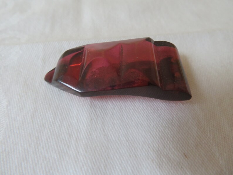 May include: A deep red, faceted glass button with a geometric shape.