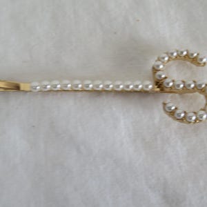 Peut inclure: Une pince à cheveux dorée avec un motif de perles en forme de lettre "S".