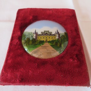 Peut inclure: Une boîte en velours rouge avec un médaillon rond en porcelaine blanche représentant une image peinte à la main du château d'Inveraray. Le château est jaune avec des bordures blanches et est entouré d'arbres verts. Le texte "Inveraray Castle" est imprimé sous l'image.