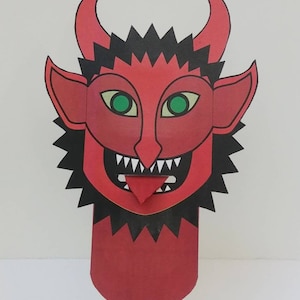 May include: Red and black paper puppet of a devil with a large grin and green eyes. The puppet is attached to a wooden stick.