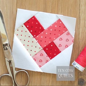May include: A handmade quilt block featuring a heart design in shades of red and pink, with white accents. The block is surrounded by white fabric and includes a pair of scissors and a spool of red thread. The text "TEN COW QUILTS" is visible.