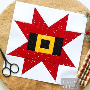 May include: A square quilt block featuring a central yellow square surrounded by a black rectangular border, set within a red star with white speckles on a white background. The block includes the text Ten Cow Quilts in the bottom corner.
