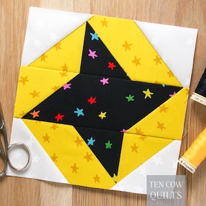 以下が含まれることがあります： 星のデザインが施された、完成したキルトブロック。中央の星は、カラフルな星が散りばめられた黒色で、黄色の星柄の生地で囲まれています。白い星柄の白い生地が背景を形成しています。ハサミと糸巻きも写っています。「TEN COW QUILTS」の文字が右下にあります。