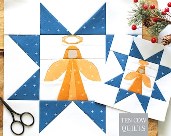 Könnte beinhalten: Zwei quadratische Quiltblöcke mit einer zentralen goldenen Engelsfigur mit Heiligenschein, umgeben von einem blauen Sternmuster mit weißen Pluszeichen auf weißem Grund. Die Blöcke sind mit einer schwarzen Schere und einem Tannenzweig abgebildet.