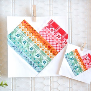 Pode incluir: Duas peças de tecido em forma de coração de patchwork, uma maior que a outra, estão presas a um fundo branco. O tecido é um arco-íris de cores, incluindo vermelho, laranja, amarelo, verde, azul e rosa. O tecido tem uma variedade de padrões, incluindo xadrez, bolinhas e flores.