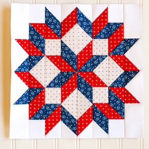 Pode incluir: Um bloco de colcha vermelho, branco e azul com um padrão de estrela. O bloco é composto por quadrados e triângulos, e as cores são dispostas em um padrão simétrico.