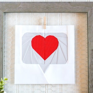 Puede incluir: Una tarjeta blanca con un corazón rojo en el centro, enmarcada en un marco de madera con un respaldo de malla metálica.