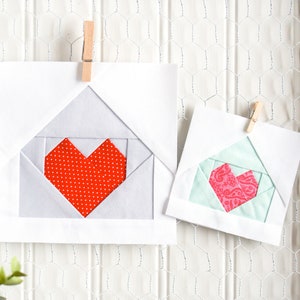 Peut inclure: Deux blocs de courtepointe en tissu en forme de cœur faits à la main, l'un avec un cœur rouge à pois blancs et l'autre avec un cœur rose à motif cachemire, sont affichés sur un fond de grillage métallique blanc.