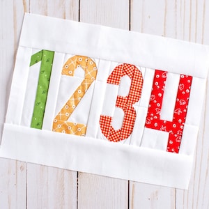 May include: A white fabric panel with the numbers 1, 2, 3, and 4 sewn on in different colored fabrics. The number 1 is green, the number 2 is yellow, the number 3 is red, and the number 4 is red with white polka dots.