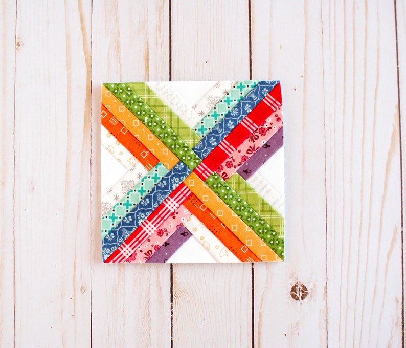 K&ouml;nnte beinhalten: Ein farbenfroher Patchwork-Quiltblock mit einem Kreuzmuster. Der Block besteht aus verschiedenen Stoffen in Rot-, Orange-, Gelb-, Gr&uuml;n-, Blau- und Violett&ouml;nen.