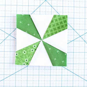 May include: A white fabric square with eight green fabric triangles sewn around the edges. The triangles have different patterns, including small white flowers, small white diamonds, and white crosses.