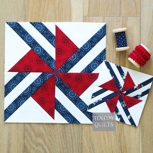 May include: Two square quilt blocks featuring a pinwheel design in red, white, and dark blue with floral and star patterns. A wooden spool with dark blue fabric and a wooden spool with red pom-pom trim are included. Text reads TEN COW QUILTS.