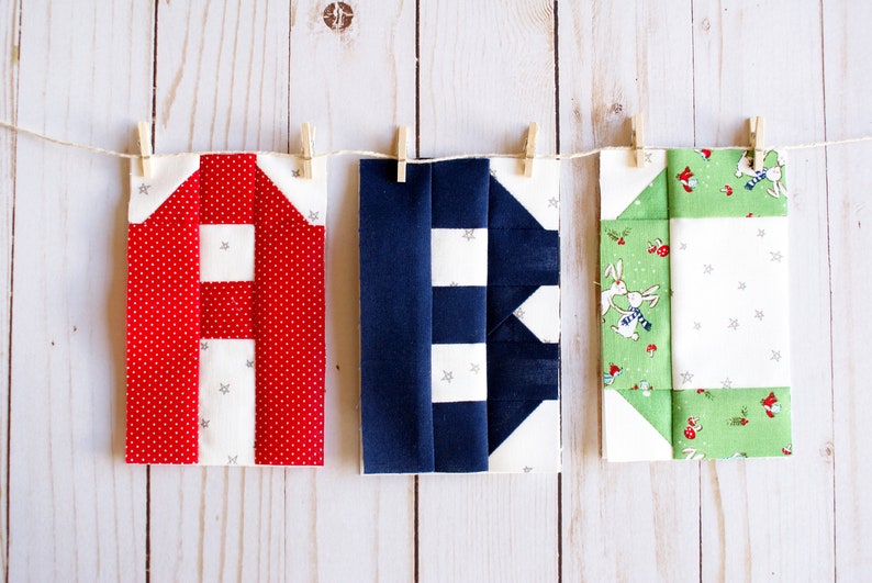 May include: Three fabric squares with different patterns are hanging on a clothesline. The square on the left is red with white polka dots and stars. The middle square is navy blue with white stripes and stars. The square on the right is green with a white background and a pattern of bunnies and flowers.