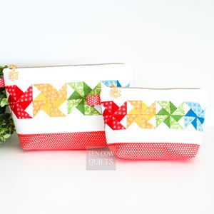 May include: Two red and white zippered pouches with a colorful pinwheel design. The pouches are made of fabric and have a red polka dot lining. The larger pouch has the text "Ten Cow Quilts" printed on the bottom.