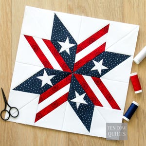 May include: A patriotic quilt block featuring a star design with red and white stripes, blue polka dot sections, and white stars. The block is on a white background with the text "TEN COW QUILTS". Scissors and spools of thread are visible.