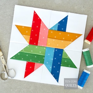 Peut inclure: Un bloc de patchwork en forme d'étoile sur fond blanc. L'étoile est composée de tissus rouges, oranges, roses, verts, bleus et blancs. Le bloc est entouré de tissu blanc. Des ciseaux et des bobines de fil sont visibles en arrière-plan.