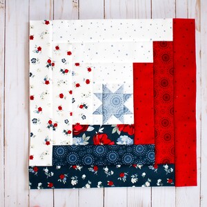May include: A red, white and blue quilt block with a star in the centre. The block is made up of different fabrics with floral and geometric patterns.