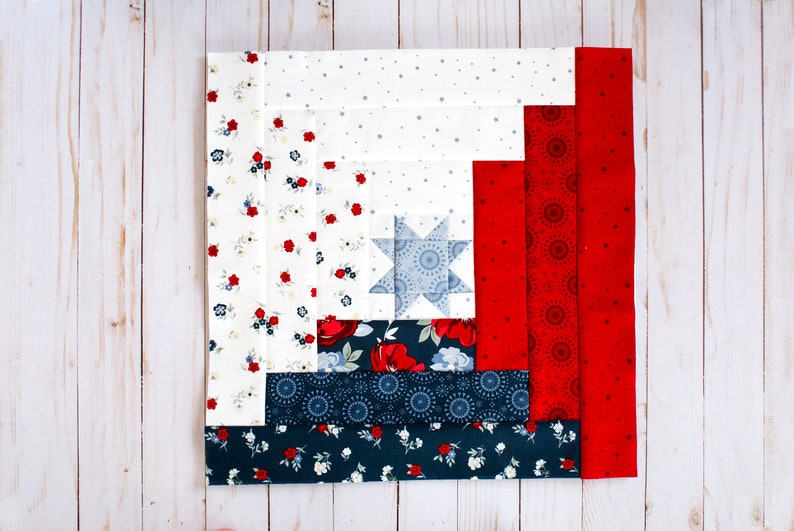 May include: A red, white and blue quilt block with a star in the centre. The block is made up of different fabrics with floral and geometric patterns.