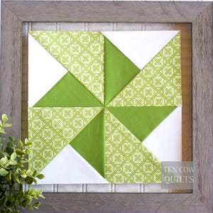 Pode incluir: Um bloco de colcha emoldurado com um design de cata-vento. A colcha apresenta tecido branco, verde liso e verde estampado. O tecido estampado tem um design geom&eacute;trico verde claro. A moldura &eacute; de cor cinza claro e o texto "TEN COW QUILTS" &eacute; vis&iacute;vel.